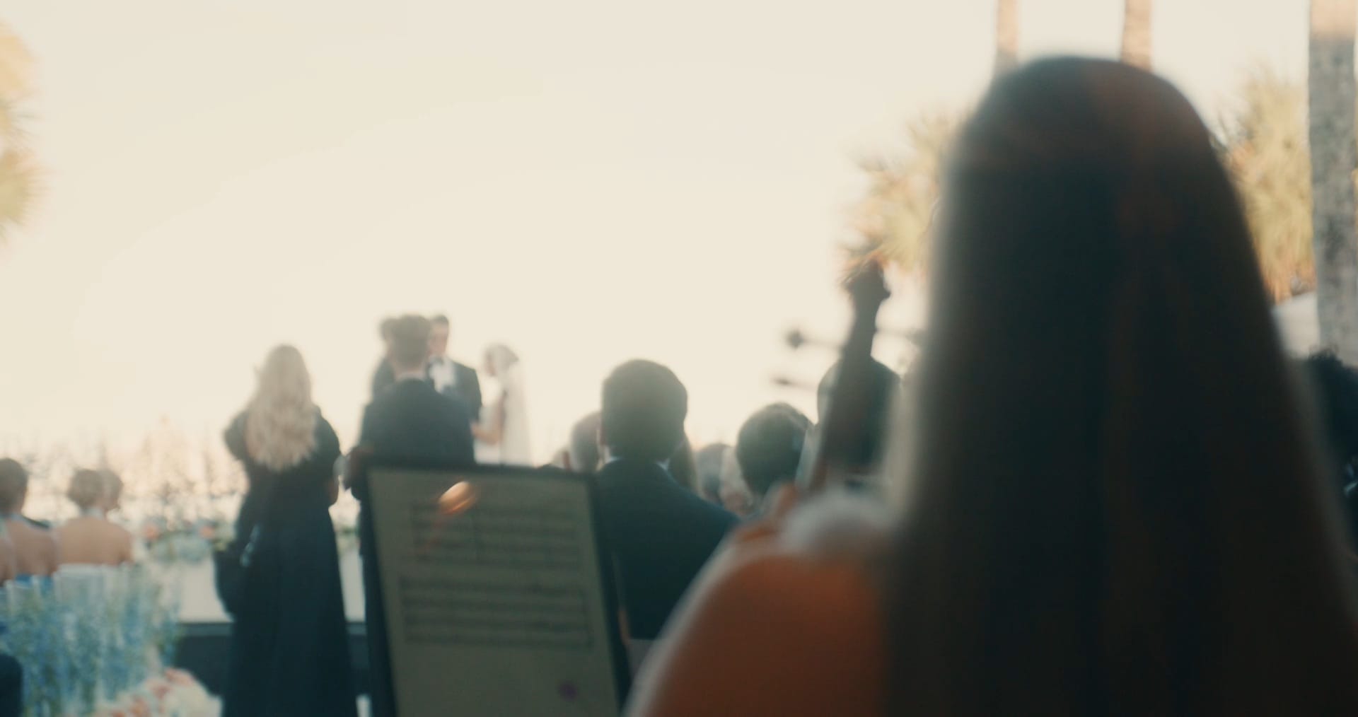 Miami wedding music violinist preparing to serenade a smiling bride and groom as they walk hand-in-hand beneath tall palm trees.
