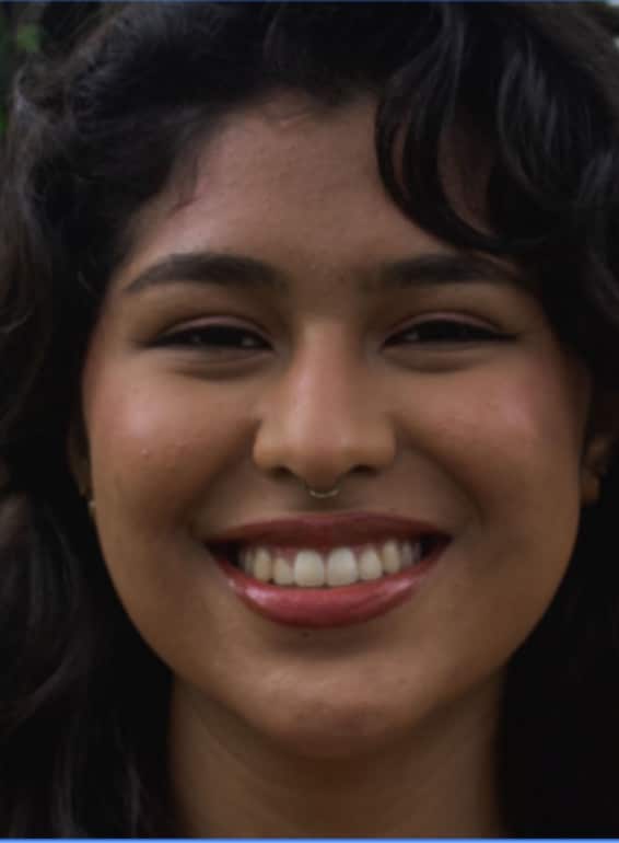Close-up portrait of a woman with long black hair, a warm smile, and a nose piercing, looking directly at the camera.