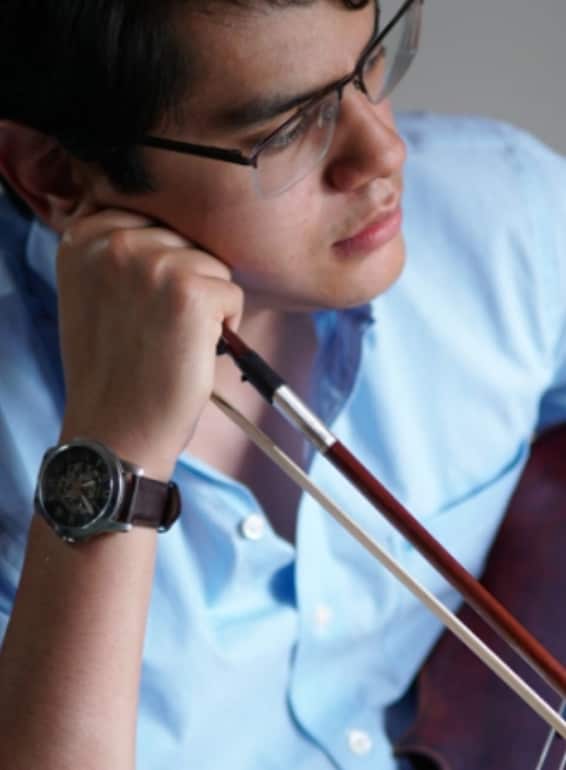 A person wearing glasses and a light blue shirt holds a paintbrush while looking thoughtfully downward, with a watch visible on their wrist.