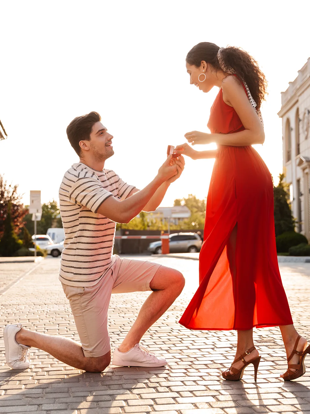 A man proposing to a woman in a red dress on the beach