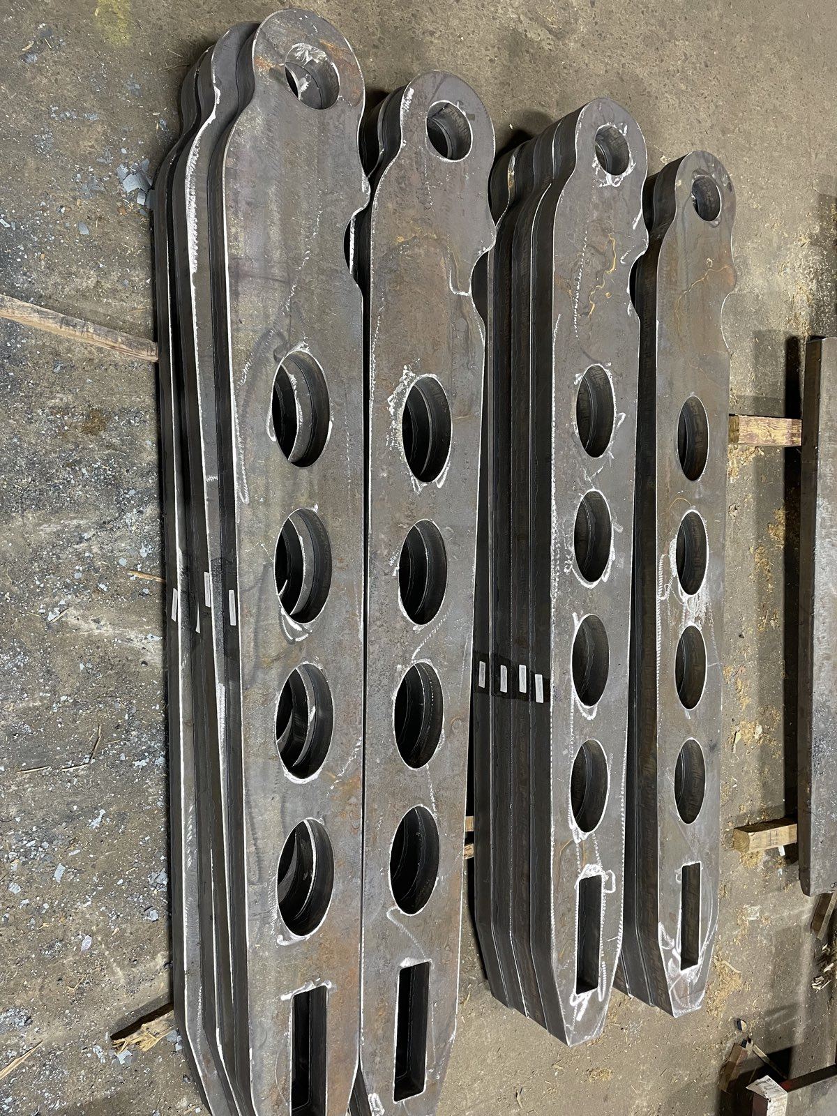 Burned steel lifting arms with bored holes, staged in sets