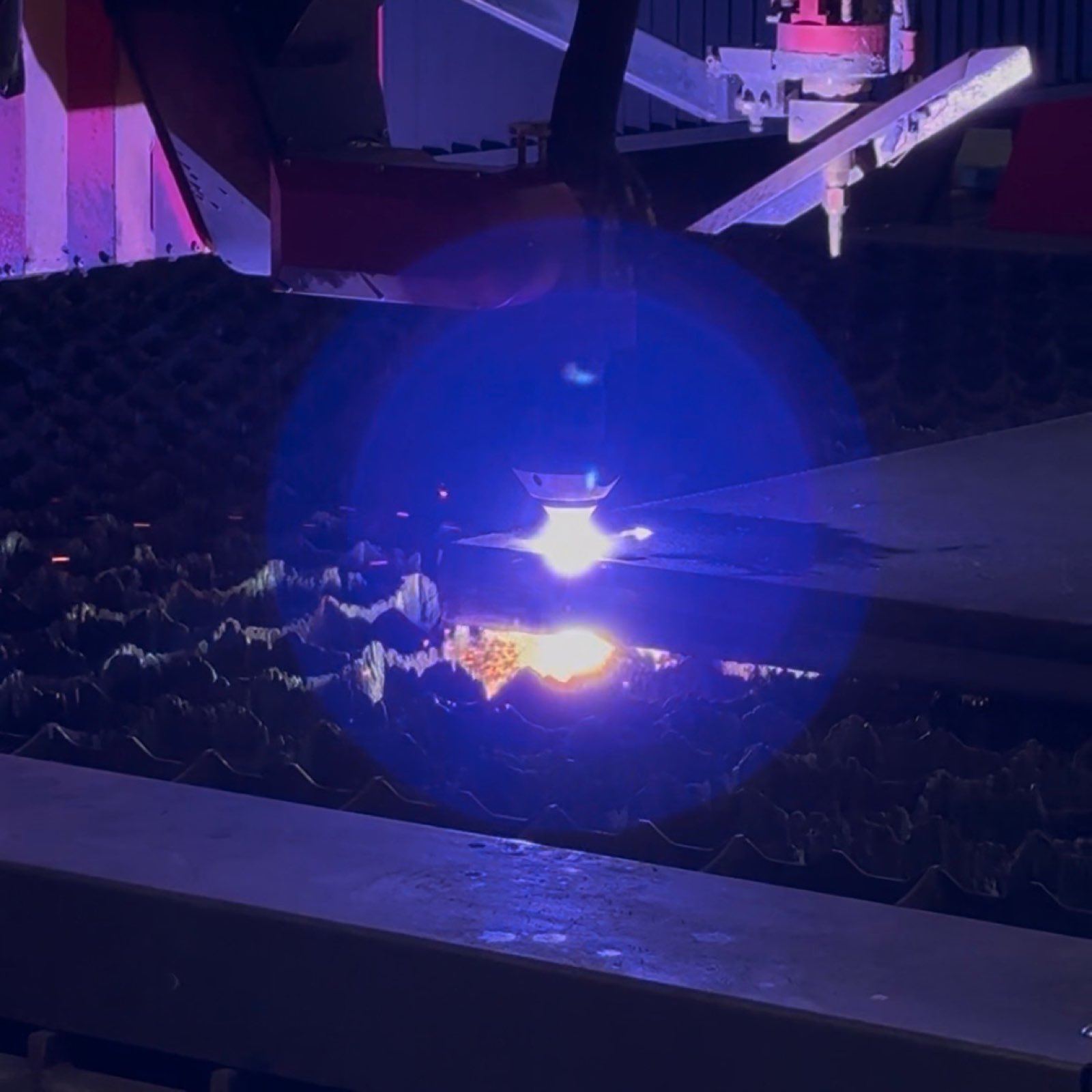 Plasma torch piercing steel plate under a bright blue arc